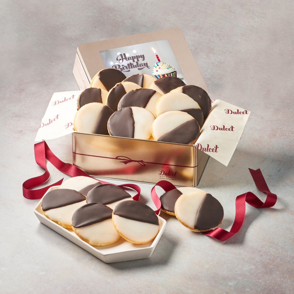 Dulcet gold birthday gift tin filled with gourmet black and white cookies featuring chocolate and vanilla icing, a Happy Birthday cupcake-themed lid, branded tissue paper, and burgundy ribbon.