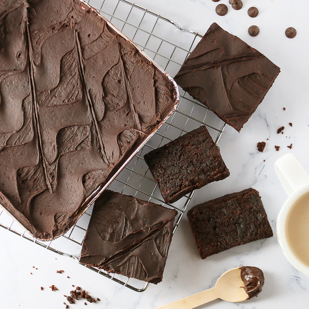 Dulcet gourmet chocolate brownies topped with smooth chocolate frosting, featuring a large brownie slab and sliced squares on a cooling rack.