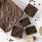 Dulcet gourmet chocolate brownies topped with smooth chocolate frosting, featuring a large brownie slab and sliced squares on a cooling rack.