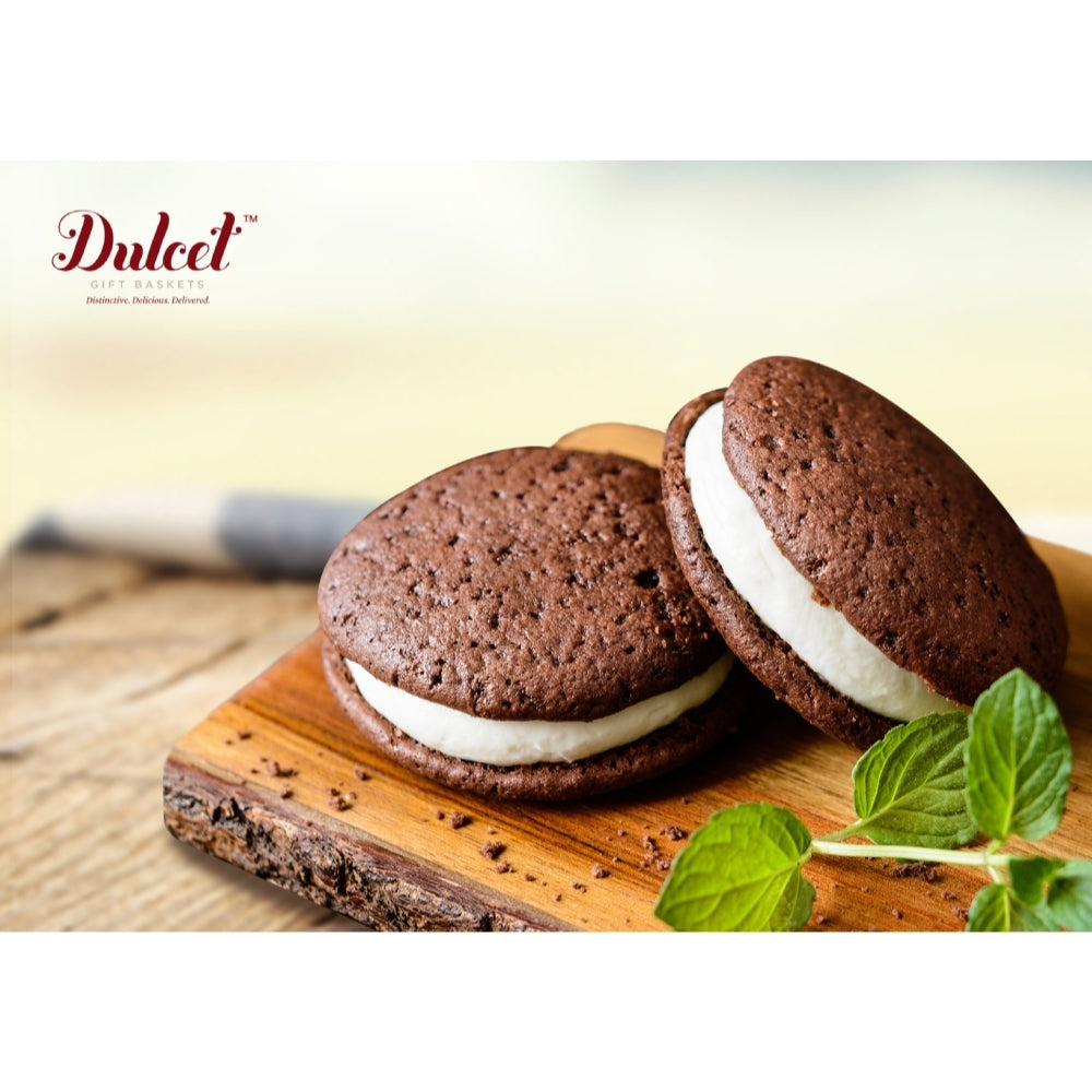 Two Dulcet chocolate whoopie pies with thick white cream filling, displayed on a rustic wooden serving board with fresh mint leaves.