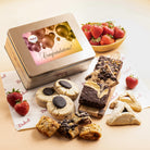 Dulcet gold congratulations gift tin featuring festive balloons and confetti, displayed with chocolate brownies, blondies, chocolate-topped cookies, hamantaschen, rugelach and fresh strawberries.