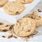 Close-up of Dulcet golden-baked oatmeal raisin cookies with visible raisins and oats, displayed on a rustic white wooden surface with broken cookie pieces.