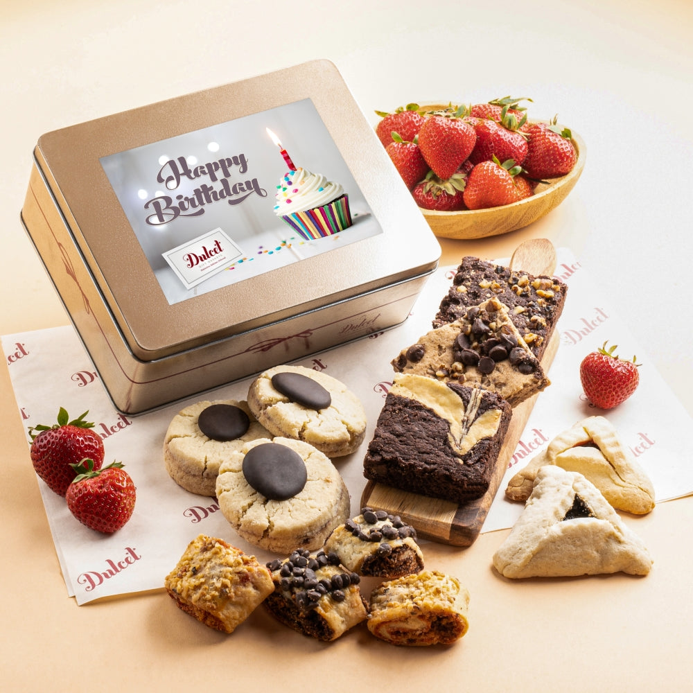 Dulcet gold Happy Birthday gift tin featuring a colorful cupcake and candle design, surrounded by assorted brownies, chocolate-topped cookies, blondies, hamantaschen, rugelach and fresh strawberries.