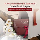 Dulcet Gift Baskets promotional image featuring a burgundy gift box with ribbon inside a white mailbox beside fresh daisies, highlighting thoughtful gift delivery to family and friends from afar.