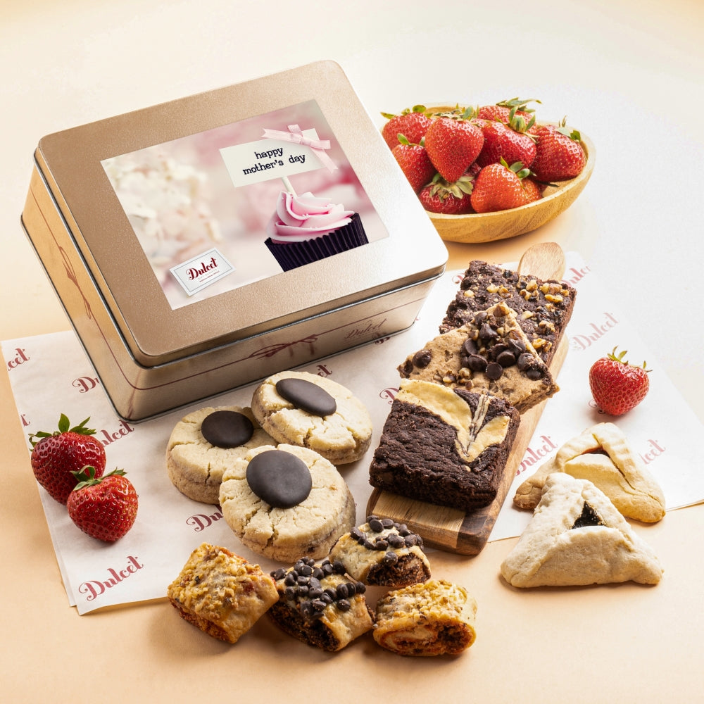 Gold Dulcet Mother's Day gift tin with a pink cupcake greeting label, surrounded by chocolate-topped cookies, brownies, blondies, hamantaschen, assorted rugelach and fresh strawberries.