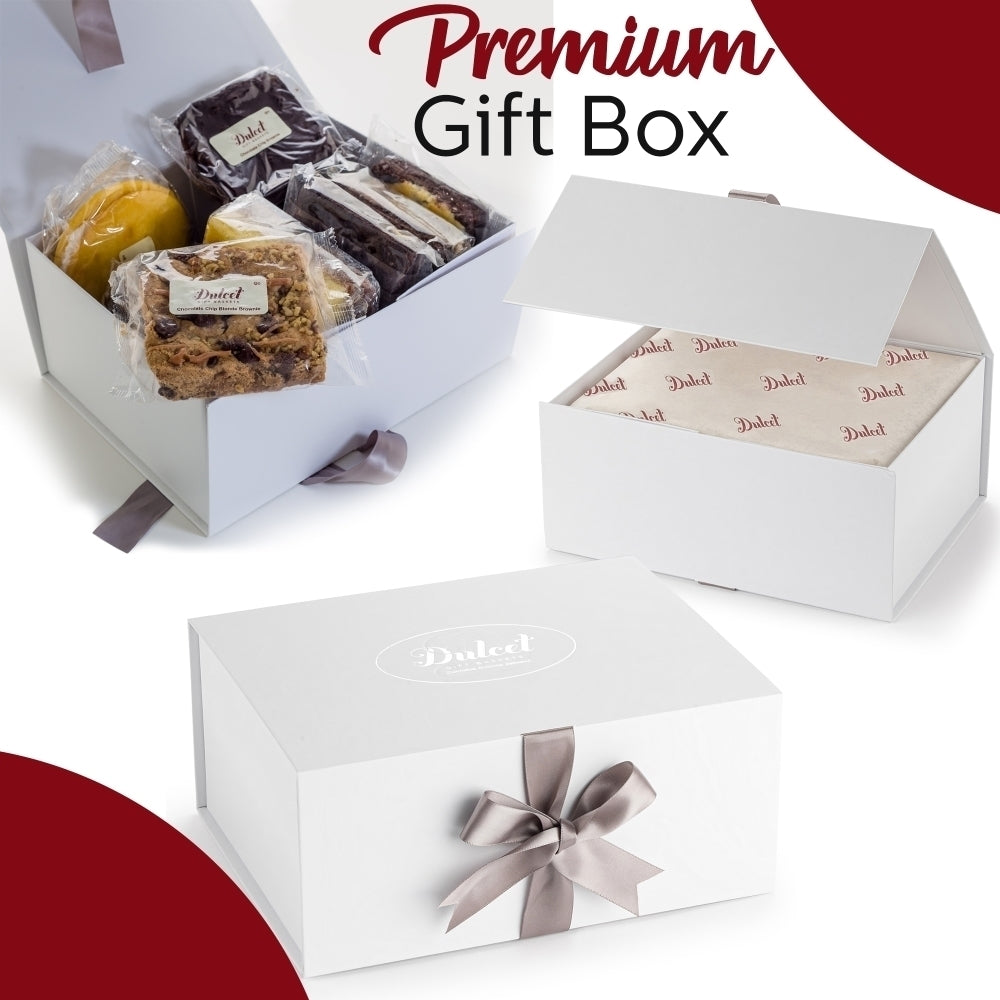 Dulcet premium white gift box shown open with individually wrapped gourmet brownies and assorted baked treats, alongside elegant packaging, branded tissue paper and a silver satin bow.