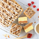 Dulcet raspberry crumb cake with golden streusel topping, white icing drizzle and raspberry filling, shown sliced on a cooling rack with fresh raspberries.