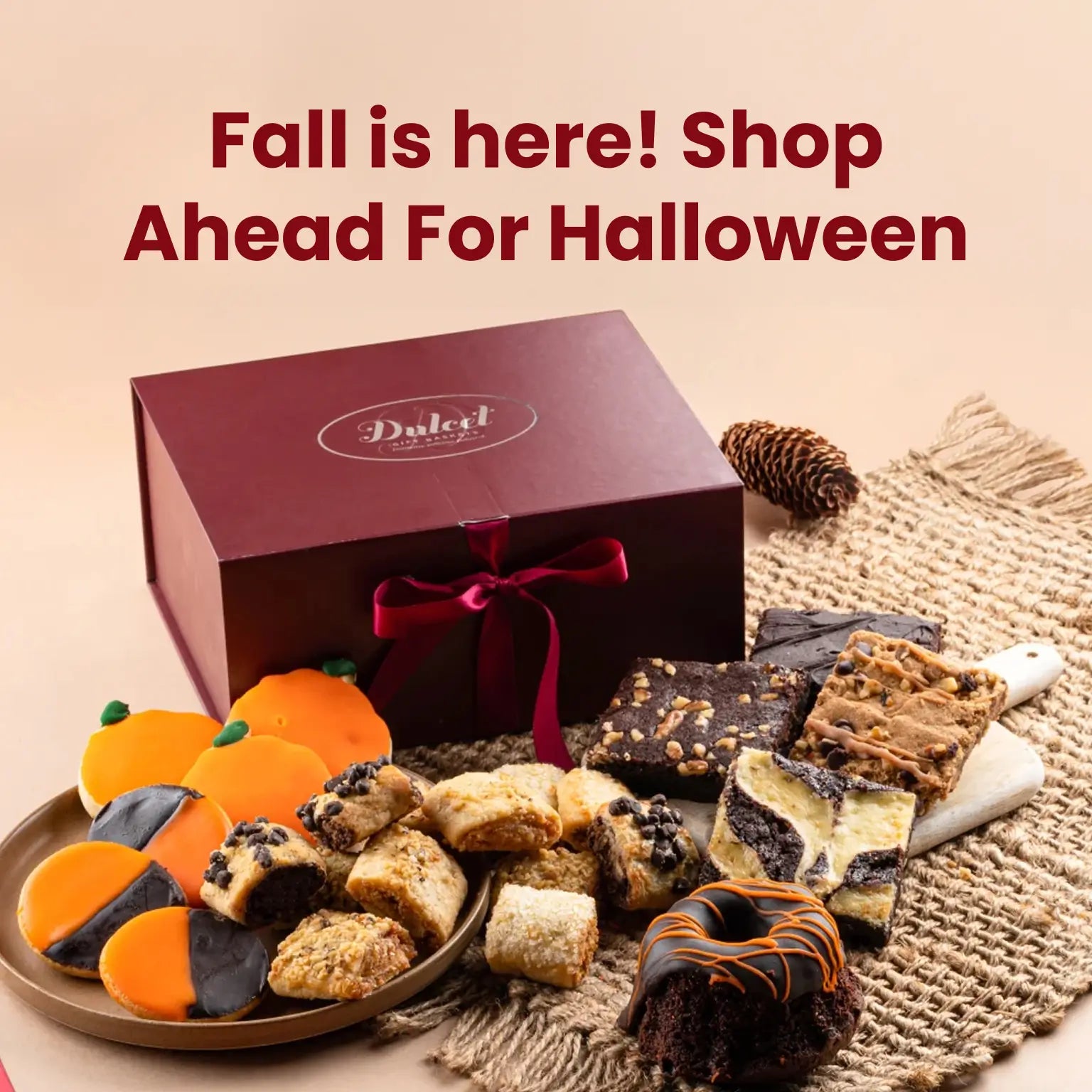 Dulcet Halloween gift basket featuring a burgundy gift box with festive orange and black cookies, assorted brownies, rugelach, and chocolate cake.