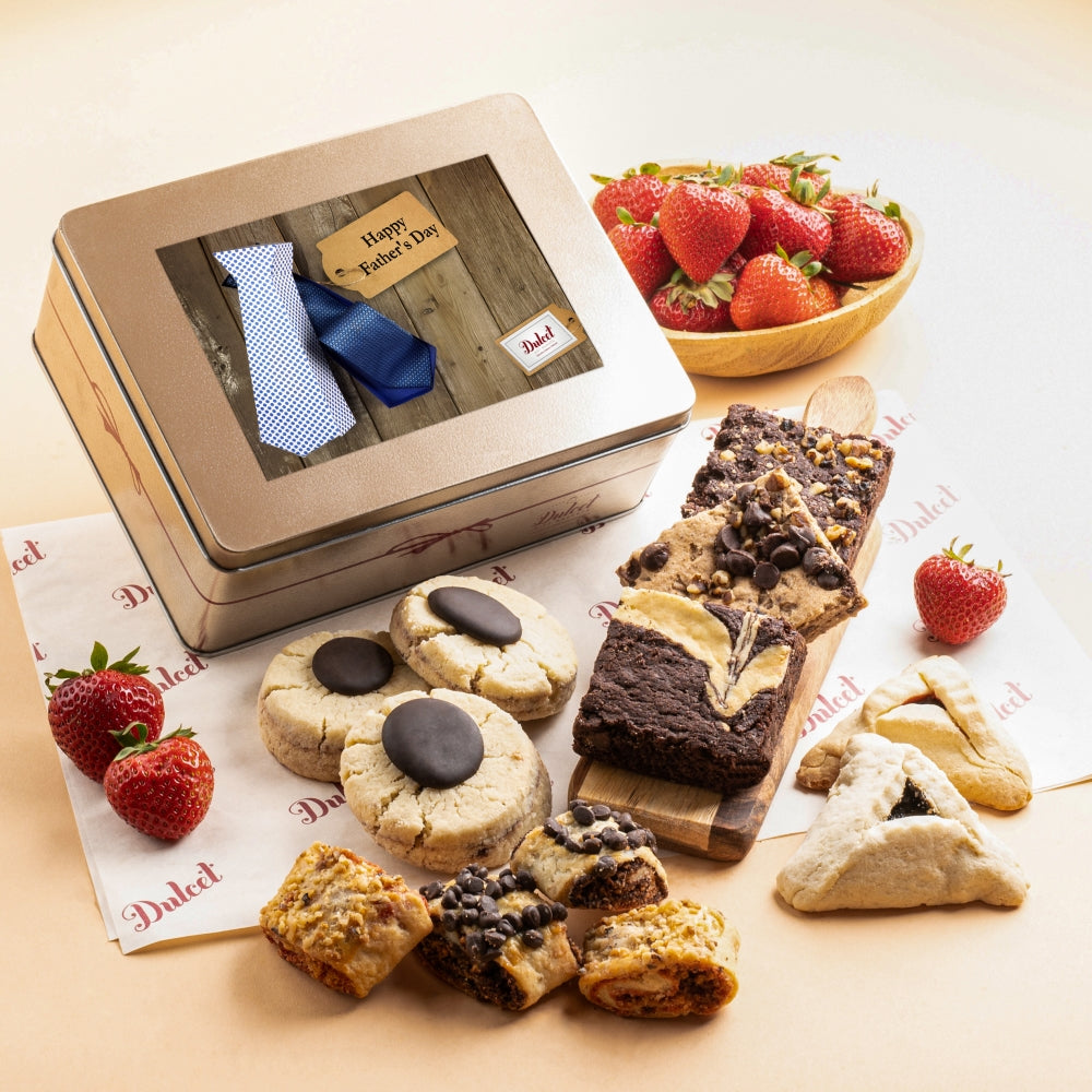 Dulcet Father's Day gold gift tin with blue necktie design, displayed alongside chocolate brownies, chocolate-topped cookies, hamantaschen, assorted rugelach and fresh strawberries.