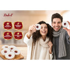 Smiling couple holding raspberry-filled Linzer cookies with powdered sugar, highlighting Dulcet's handmade quality, fine ingredients and freshly baked treats.