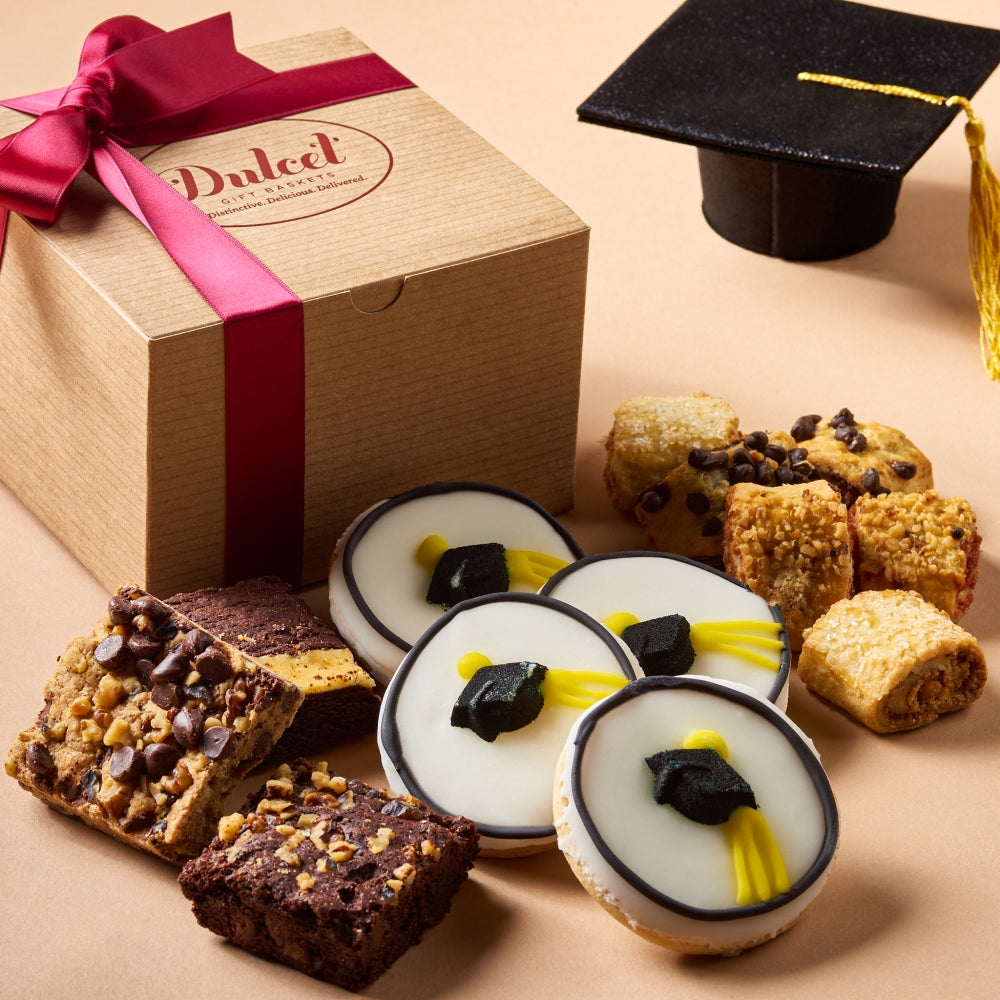 Dulcet graduation gift box with decorated graduation cap cookies, assorted brownies, blondies and rugelach beside a graduation cap.