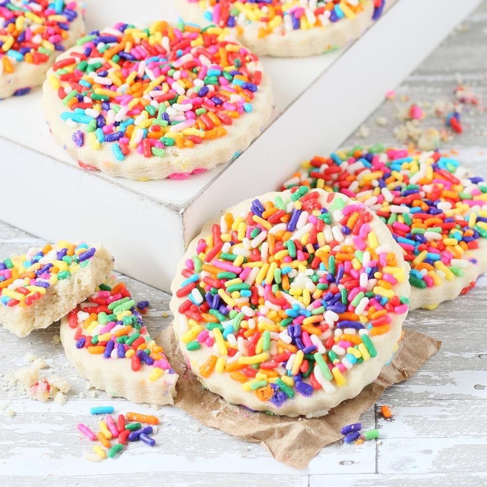 Close-up of freshly baked sugar cookies topped with colorful rainbow sprinkles, showing their buttery texture and festive decoration.