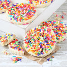 Close-up of freshly baked sugar cookies topped with colorful rainbow sprinkles, showing their buttery texture and festive decoration.