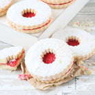 Close-up of raspberry jam-filled Linzer sandwich cookies dusted with powdered sugar, featuring golden buttery cookie layers and red fruit filling.
