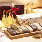 Tea Forté Herbal Retreat tea gift box with pyramid tea infusers, assorted chocolate-dipped biscotti on a wooden tray and a burgundy gift box with red ribbon.