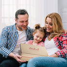 Parents and their young daughter smiling together while holding a Dulcet bakery gift box.