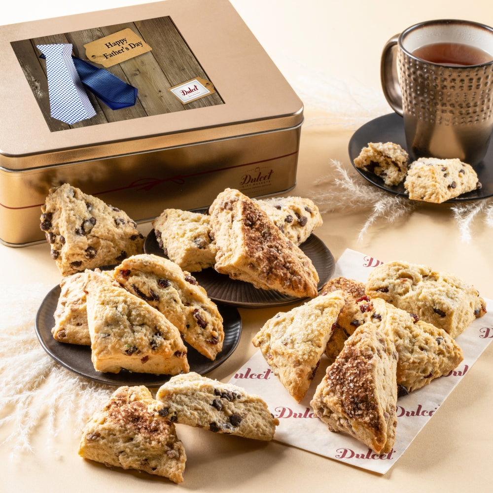 Assorted scones displayed with a Dulcet gold Father’s Day gift tin featuring a necktie design and a mug of tea.