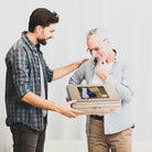 A younger man presents a Dulcet Father’s Day gold gift tin to a smiling older man.