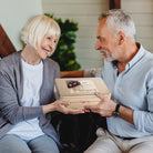 An older couple smiling while holding a Dulcet bakery gift box together.